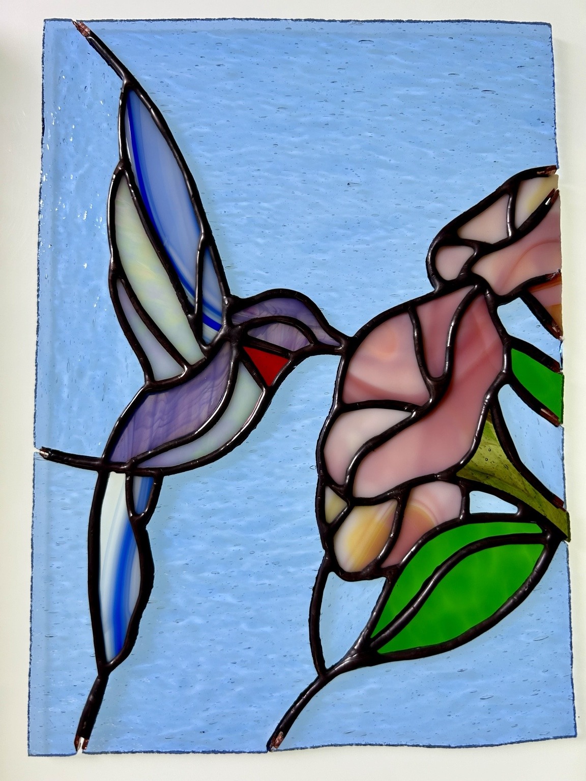 A hummingbird beside a pink bloom in a blue glass panel.