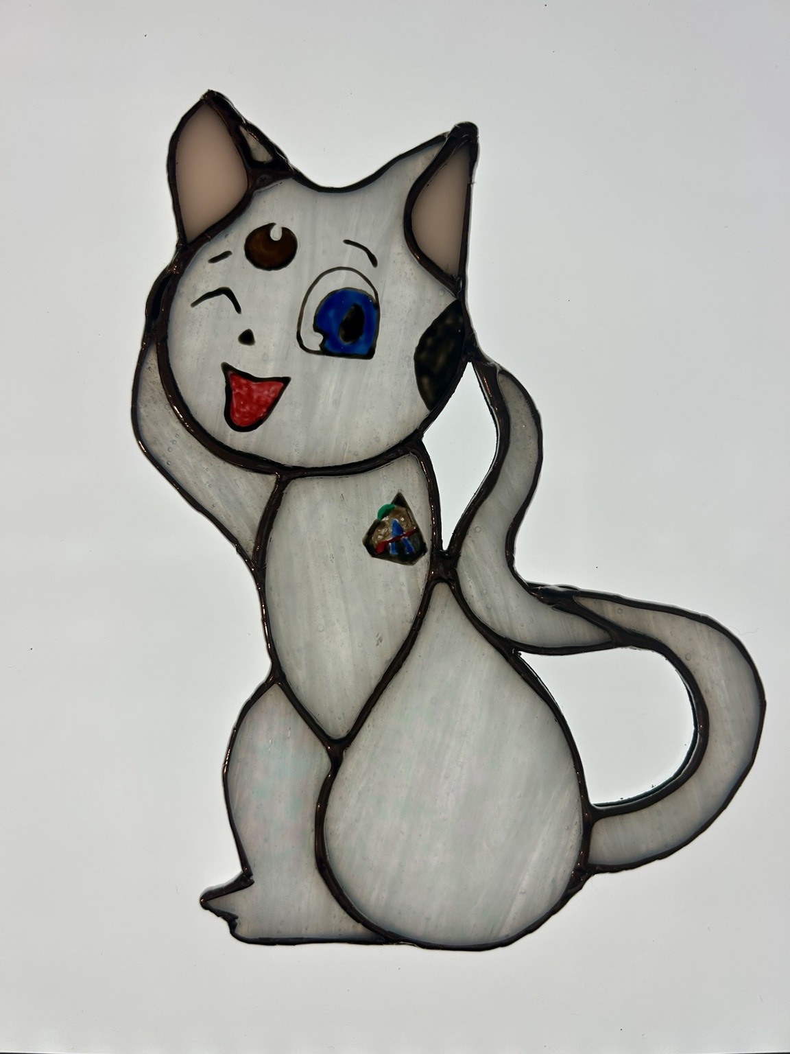 A playful pale-glass cat with a blue eye and a curling tail.